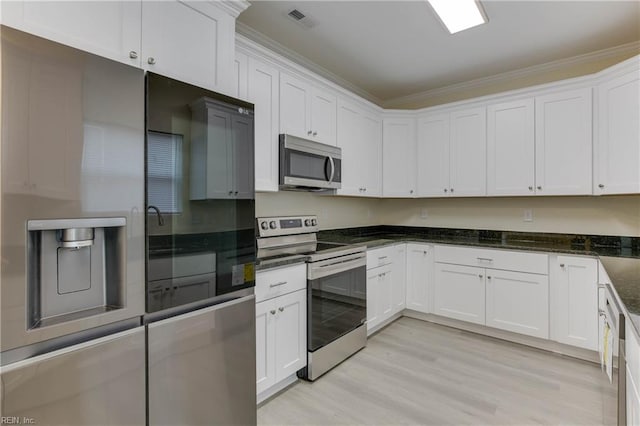 kitchen with dark stone counters, light hardwood / wood-style floors, white cabinets, stainless steel appliances, and crown molding