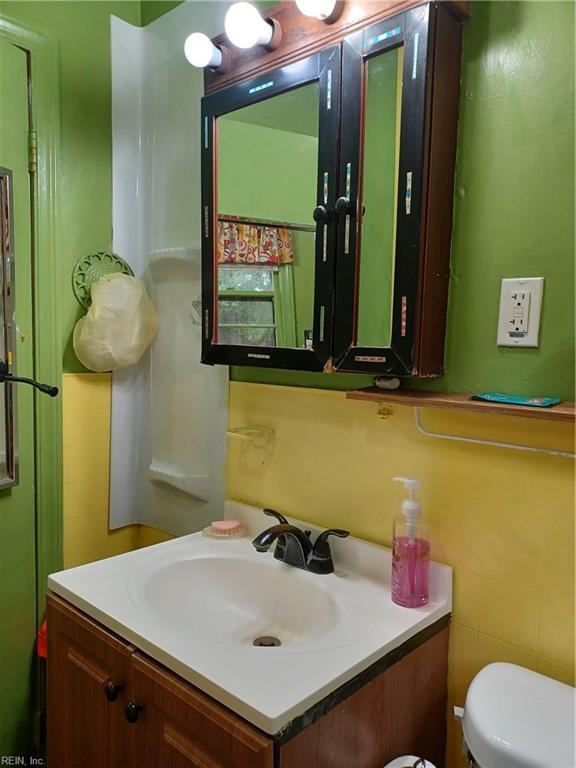 bathroom with toilet, vanity, and tile walls