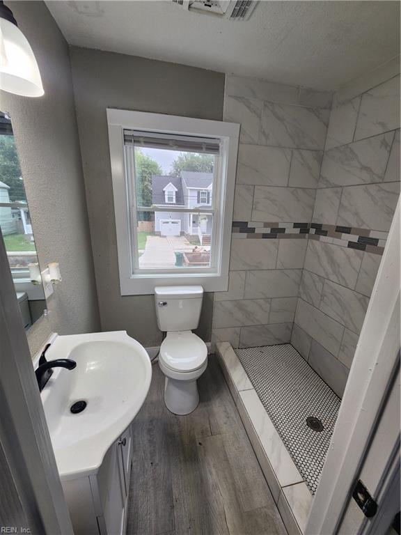 bathroom with a tile shower, vanity, hardwood / wood-style floors, and toilet