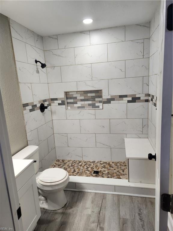 bathroom featuring vanity, hardwood / wood-style flooring, toilet, and tiled shower