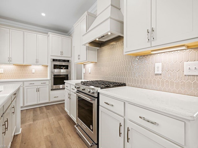 kitchen with light wood-style flooring, custom range hood, appliances with stainless steel finishes, white cabinetry, and tasteful backsplash