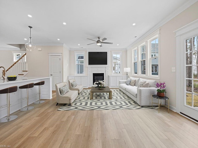 living area with stairway, wood finished floors, ornamental molding, and a fireplace