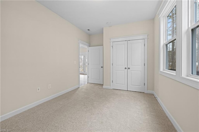 unfurnished bedroom featuring light carpet, multiple windows, a closet, and baseboards