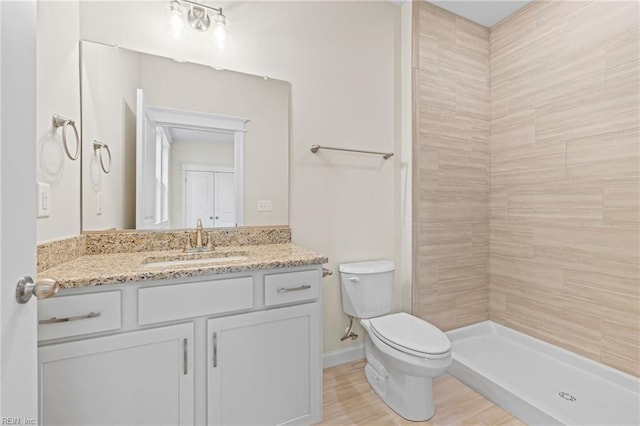 bathroom featuring toilet, wood finished floors, a tile shower, baseboards, and vanity