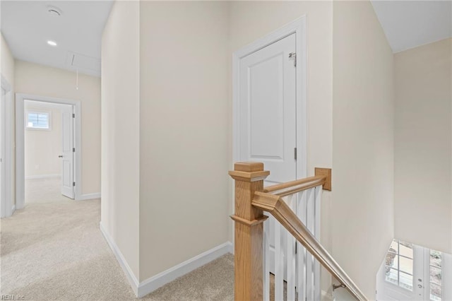 hall with baseboards, an upstairs landing, attic access, and light carpet