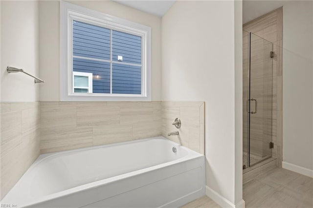 full bathroom with baseboards, a bath, and a shower stall