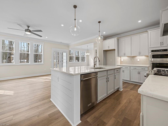 kitchen with a sink, stainless steel appliances, wood-type flooring, crown molding, and tasteful backsplash