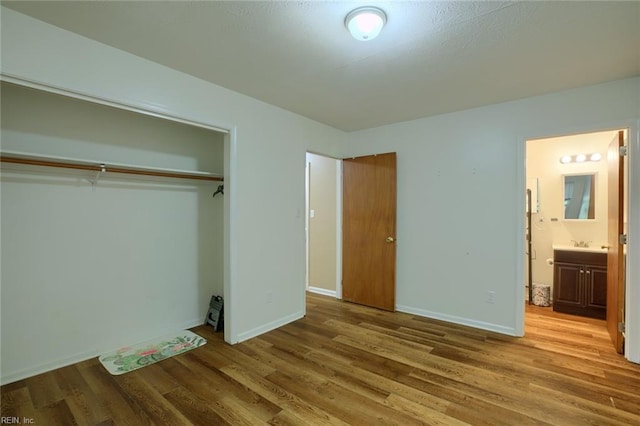 unfurnished bedroom featuring wood-type flooring, sink, ensuite bathroom, and a closet