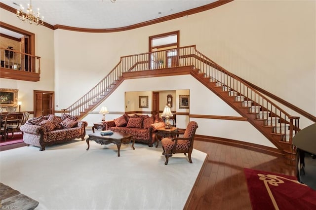 living room featuring a towering ceiling, hardwood / wood-style flooring, crown molding, and an inviting chandelier