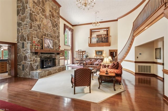 living room featuring wood-type flooring, a fireplace, an inviting chandelier, crown molding, and a high ceiling