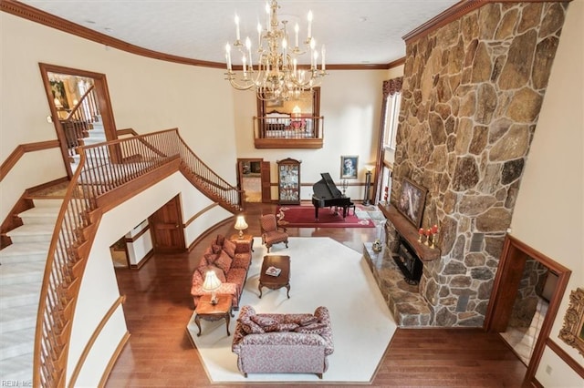 interior space with wood-type flooring, a stone fireplace, crown molding, and an inviting chandelier