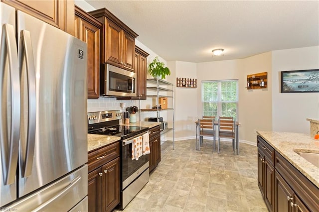 kitchen featuring decorative backsplash, stainless steel appliances, and light stone counters