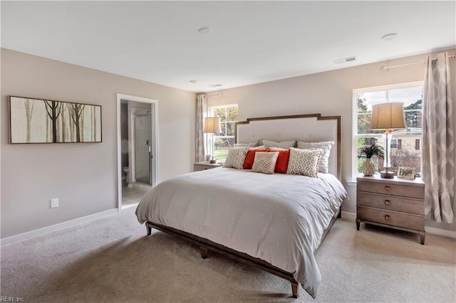 bedroom featuring light colored carpet, ensuite bathroom, and multiple windows