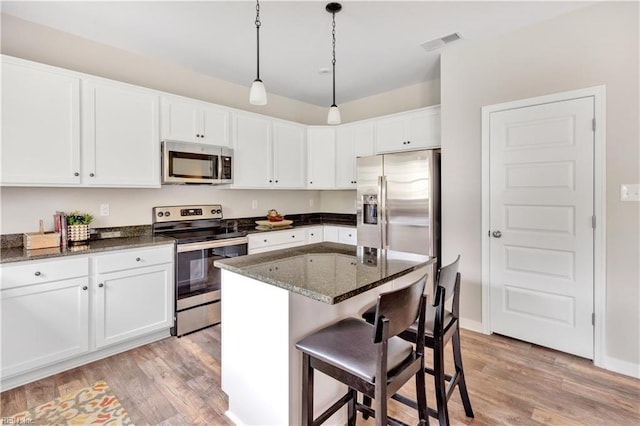 kitchen with appliances with stainless steel finishes, dark stone countertops, white cabinets, a kitchen island, and light hardwood / wood-style flooring