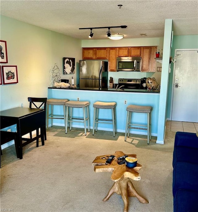 kitchen with a breakfast bar, a textured ceiling, kitchen peninsula, light colored carpet, and stainless steel appliances