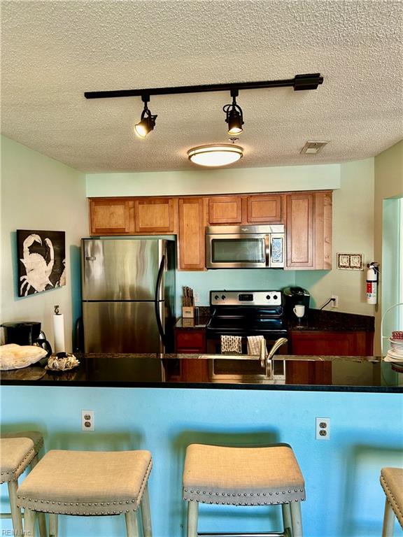 kitchen with a textured ceiling, appliances with stainless steel finishes, a kitchen breakfast bar, and rail lighting