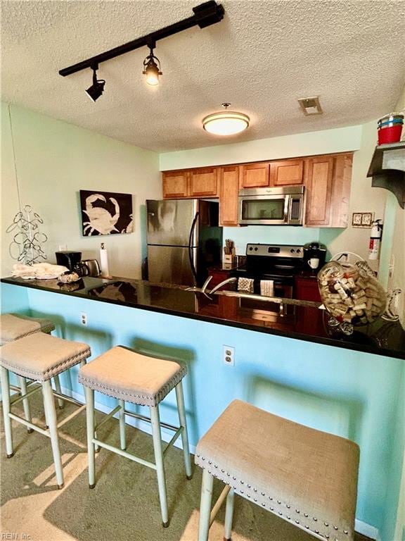 kitchen featuring a textured ceiling, stainless steel appliances, kitchen peninsula, and a kitchen breakfast bar