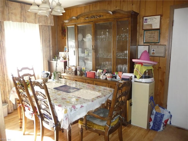 dining space featuring light hardwood / wood-style floors, wood walls, and a chandelier