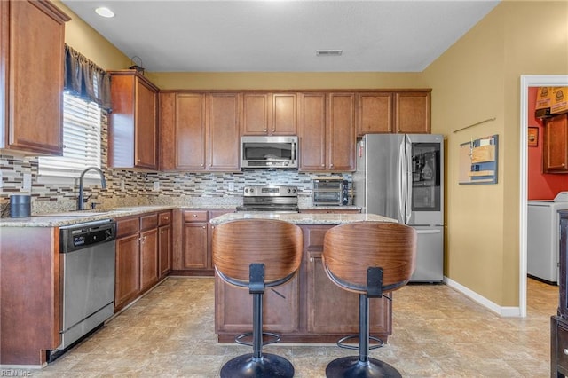 kitchen with appliances with stainless steel finishes, sink, washer / dryer, a center island, and a breakfast bar area