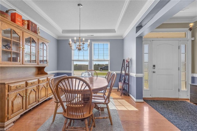 dining room with a notable chandelier, light hardwood / wood-style floors, a raised ceiling, and crown molding