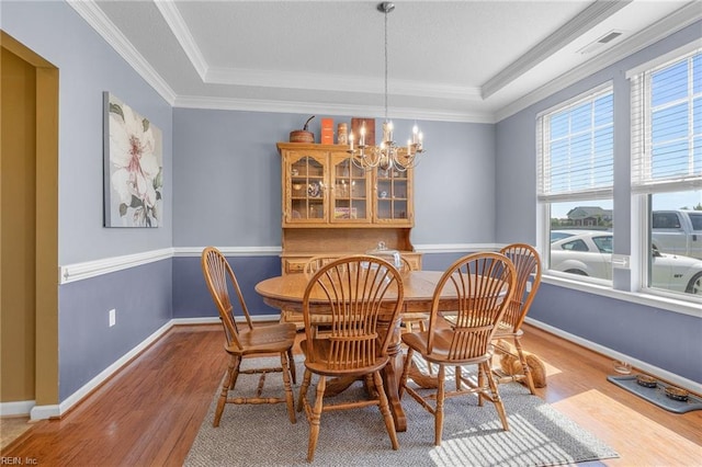 dining room with light hardwood / wood-style floors, a raised ceiling, crown molding, and a chandelier