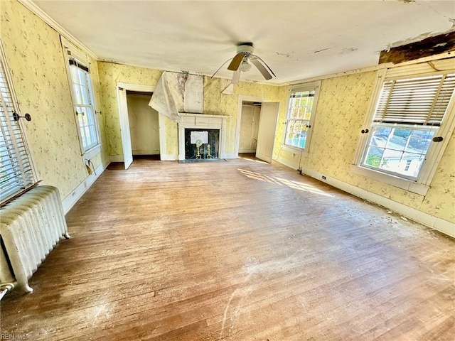 unfurnished living room with wood-type flooring, radiator, ornamental molding, and ceiling fan