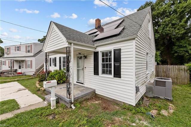 view of front of home with solar panels, central AC unit, and a front yard