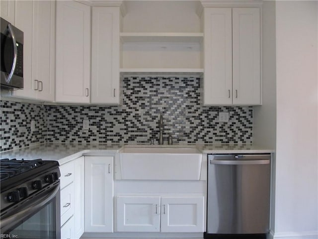 kitchen featuring light stone countertops, stainless steel appliances, sink, white cabinetry, and backsplash