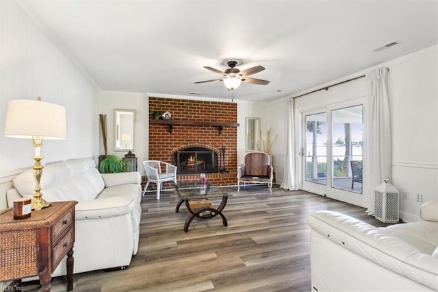 living room with a brick fireplace, dark hardwood / wood-style floors, crown molding, and ceiling fan