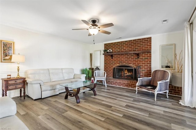 living room featuring a brick fireplace, hardwood / wood-style flooring, ornamental molding, and ceiling fan