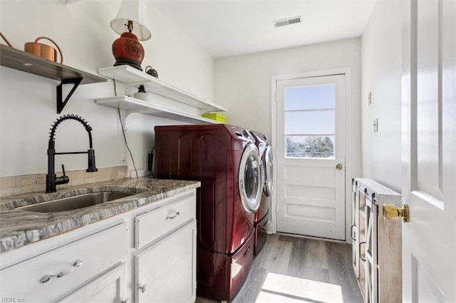 laundry area with light wood-type flooring, separate washer and dryer, sink, and cabinets