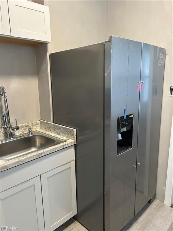 kitchen featuring white cabinets, light hardwood / wood-style floors, stainless steel fridge, and sink