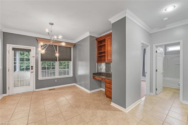 kitchen with an inviting chandelier, built in desk, ornamental molding, and decorative backsplash