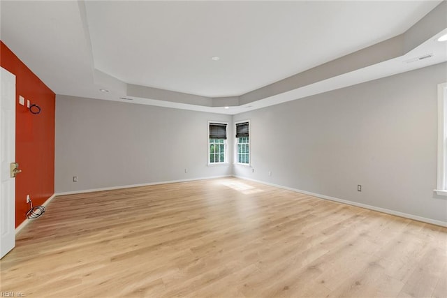 spare room featuring a tray ceiling and light hardwood / wood-style flooring