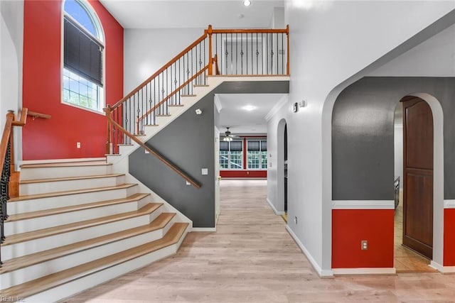 staircase with a towering ceiling, ceiling fan, and hardwood / wood-style floors