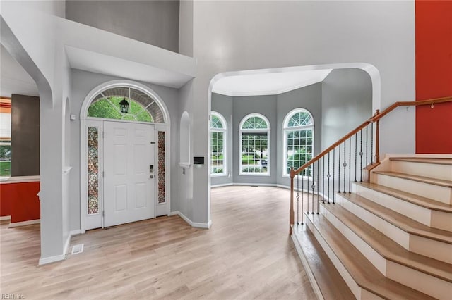 entryway featuring ornamental molding, light wood-type flooring, and a high ceiling