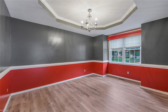 unfurnished room with ornamental molding, a tray ceiling, hardwood / wood-style flooring, and an inviting chandelier