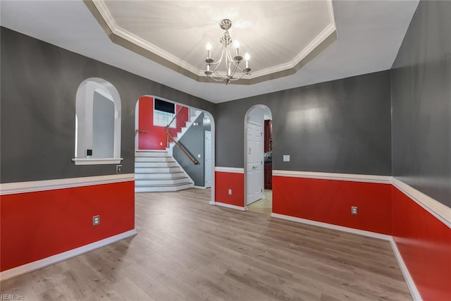 empty room with a notable chandelier, ornamental molding, a tray ceiling, and hardwood / wood-style flooring