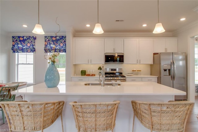 kitchen featuring appliances with stainless steel finishes, a center island with sink, hanging light fixtures, and white cabinets