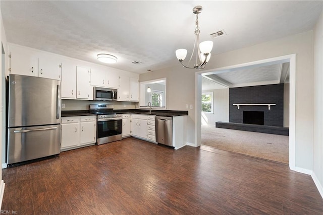 kitchen featuring dark hardwood / wood-style floors, stainless steel appliances, white cabinets, a fireplace, and decorative light fixtures