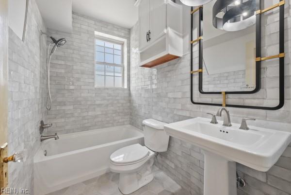 bathroom featuring toilet, backsplash, tiled shower / bath, and tile walls