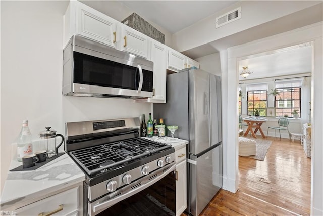 kitchen featuring white cabinets, appliances with stainless steel finishes, light hardwood / wood-style floors, and light stone countertops