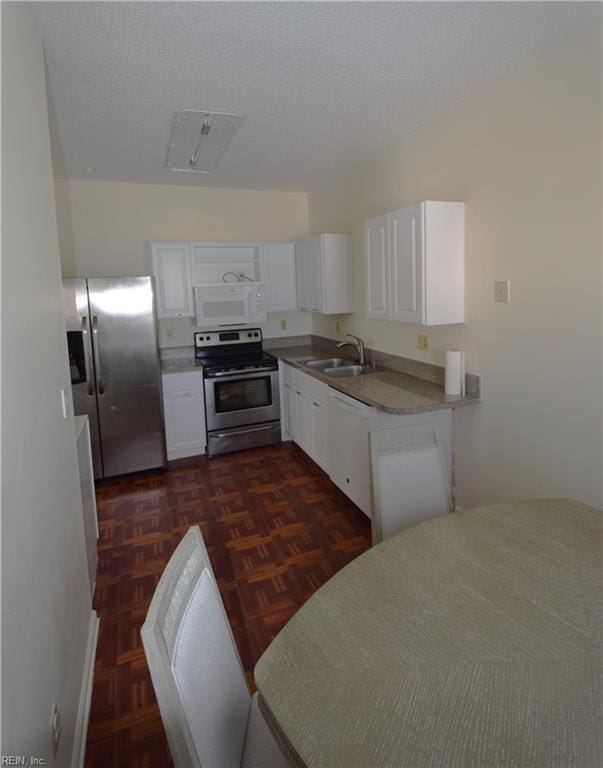 kitchen with white cabinets, dark parquet flooring, appliances with stainless steel finishes, and sink