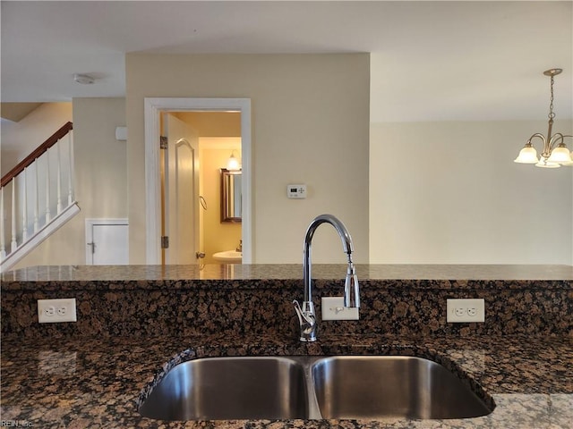 kitchen featuring decorative light fixtures, dark stone counters, a chandelier, and sink