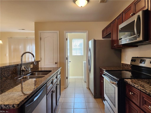 kitchen with stainless steel appliances, dark stone counters, light tile patterned flooring, and sink