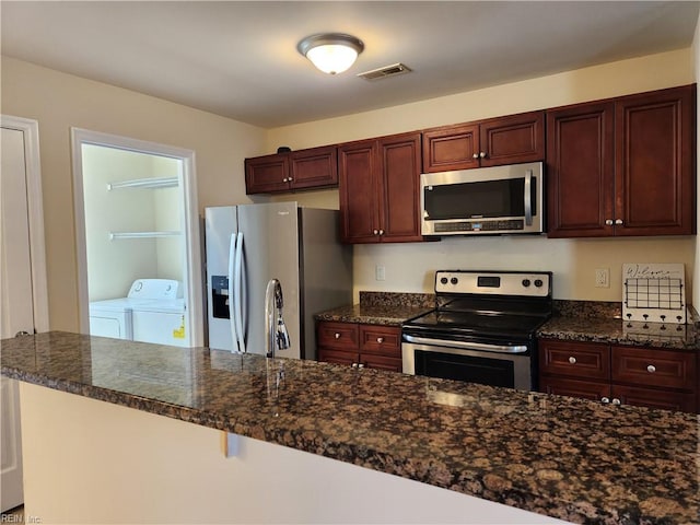 kitchen with dark stone countertops, washer and clothes dryer, sink, and stainless steel appliances