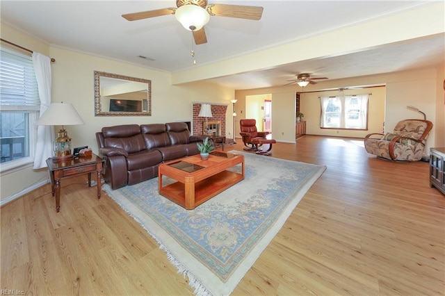 living room with ornamental molding, a brick fireplace, ceiling fan, and light hardwood / wood-style floors