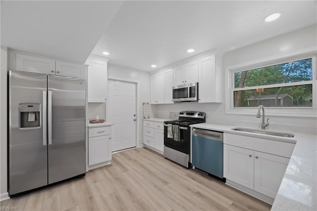 kitchen with light stone countertops, stainless steel appliances, sink, white cabinetry, and light hardwood / wood-style flooring