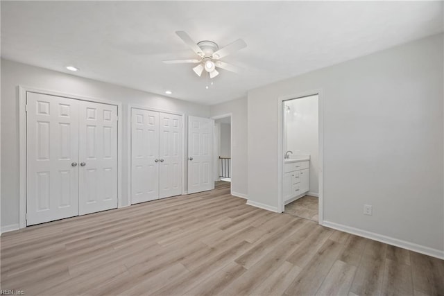 unfurnished bedroom featuring ceiling fan, multiple closets, light wood-type flooring, and ensuite bathroom