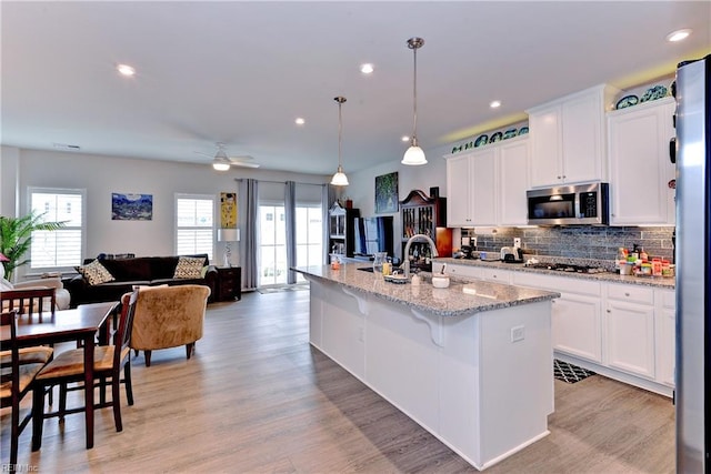 kitchen with hanging light fixtures, sink, a center island with sink, white cabinetry, and appliances with stainless steel finishes